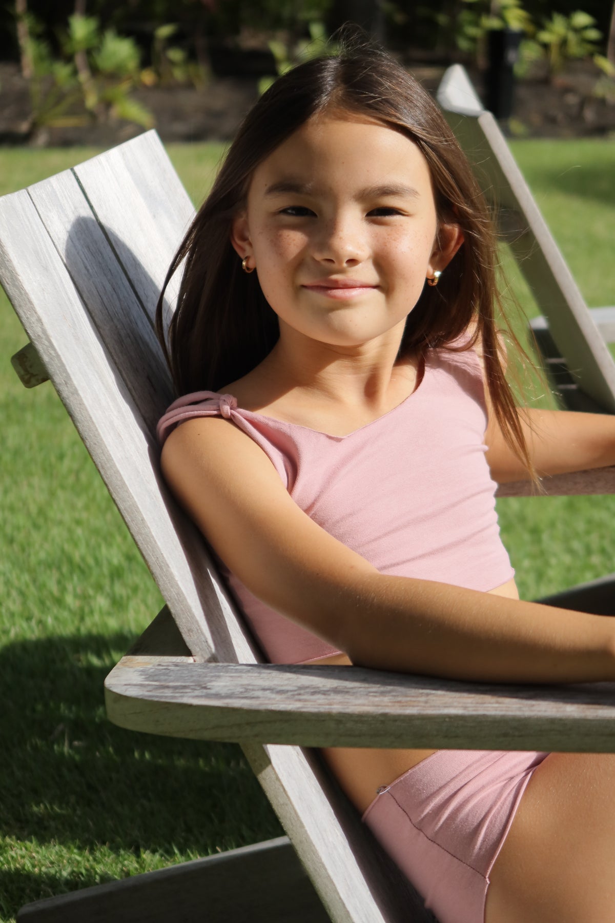Girl smiling in a rose WANINI two-piece on a wooden lounge chair in Honolulu